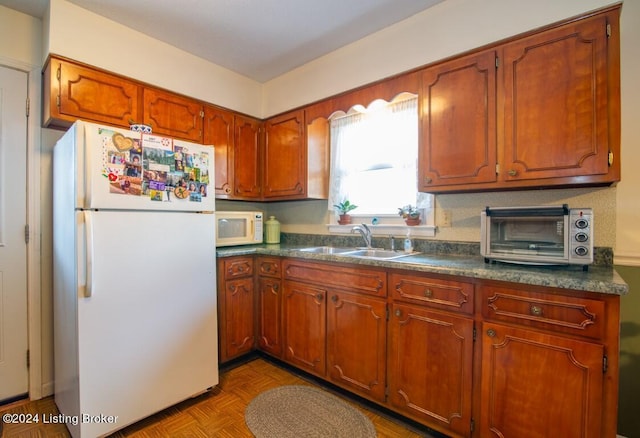 kitchen featuring white appliances, brown cabinetry, dark countertops, and a sink