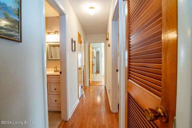 hall with a sink, baseboards, and light wood finished floors