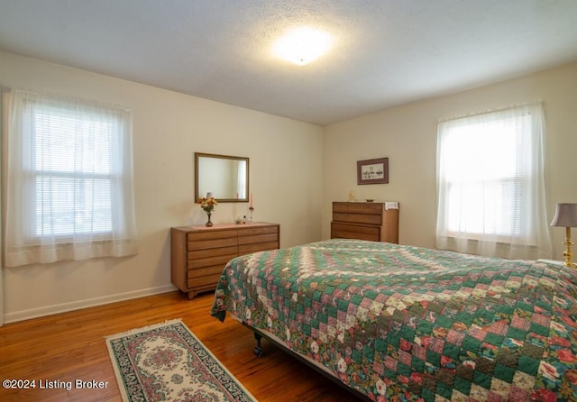 bedroom with multiple windows, wood finished floors, and baseboards