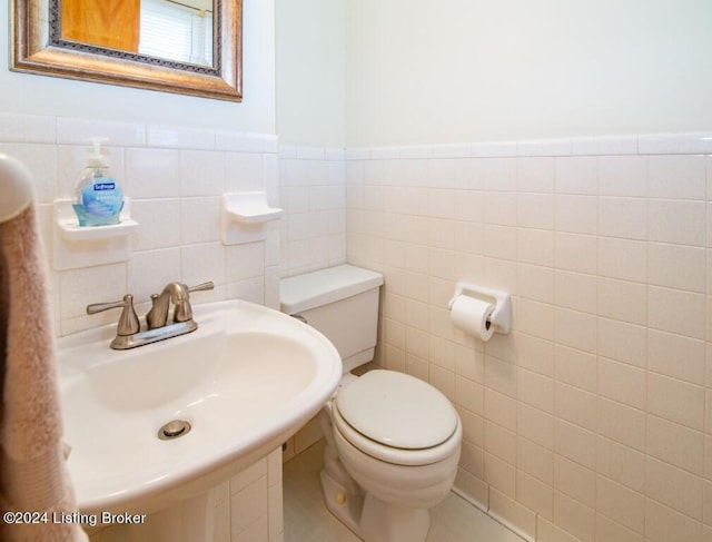 half bath featuring a wainscoted wall, toilet, tile walls, and a sink