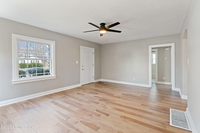 empty room featuring light wood-type flooring, visible vents, a ceiling fan, arched walkways, and baseboards