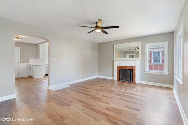 unfurnished living room featuring arched walkways, light wood-style floors, ceiling fan, and a fireplace