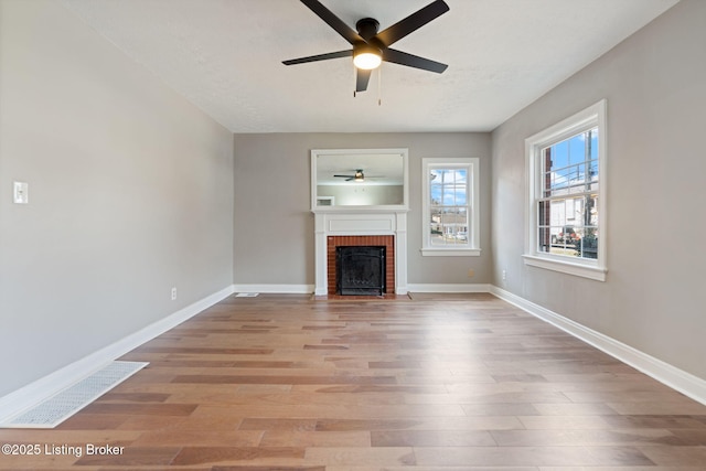 unfurnished living room with a brick fireplace, baseboards, light wood-type flooring, and ceiling fan