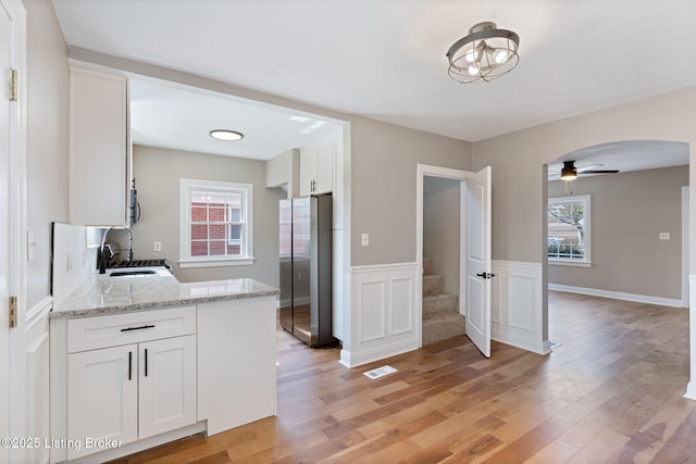 kitchen with visible vents, light wood finished floors, arched walkways, freestanding refrigerator, and a sink