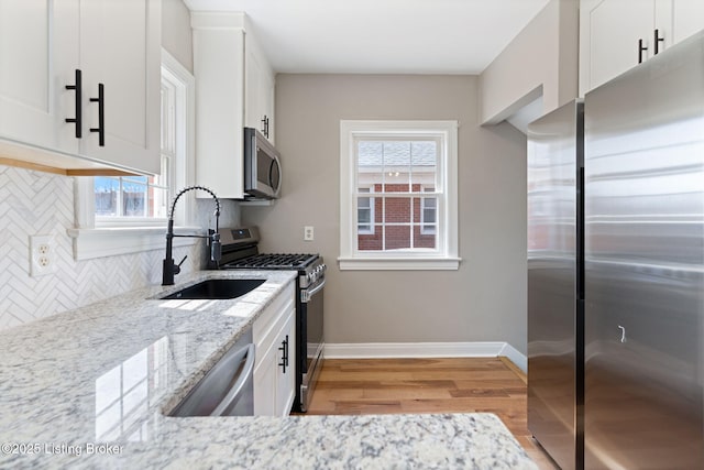 kitchen with light stone countertops, decorative backsplash, appliances with stainless steel finishes, white cabinetry, and a sink