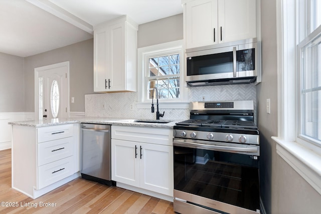 kitchen featuring light stone countertops, a sink, stainless steel appliances, light wood-style floors, and white cabinetry