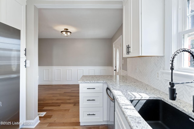 kitchen featuring light wood-type flooring, wainscoting, appliances with stainless steel finishes, white cabinetry, and a sink