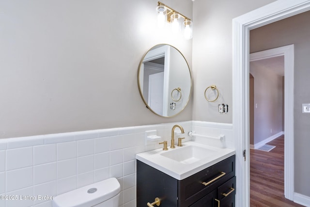 bathroom with tile walls, a wainscoted wall, toilet, wood finished floors, and vanity