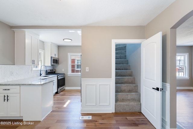 kitchen with light stone counters, a healthy amount of sunlight, stainless steel appliances, white cabinetry, and light wood-type flooring