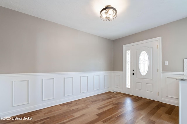 entryway with wood finished floors and a wainscoted wall