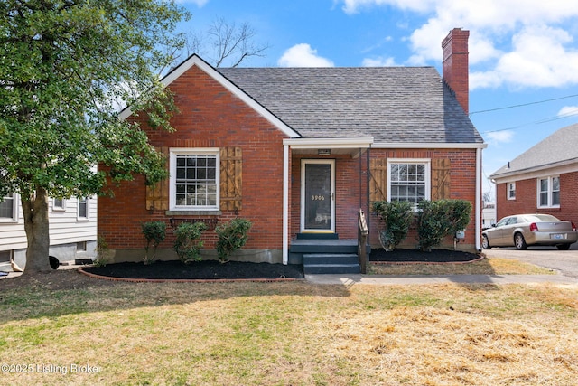 bungalow-style house with brick siding, a chimney, a front yard, and a shingled roof