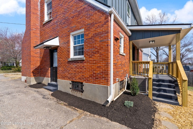 view of side of home featuring board and batten siding, cooling unit, brick siding, and a chimney