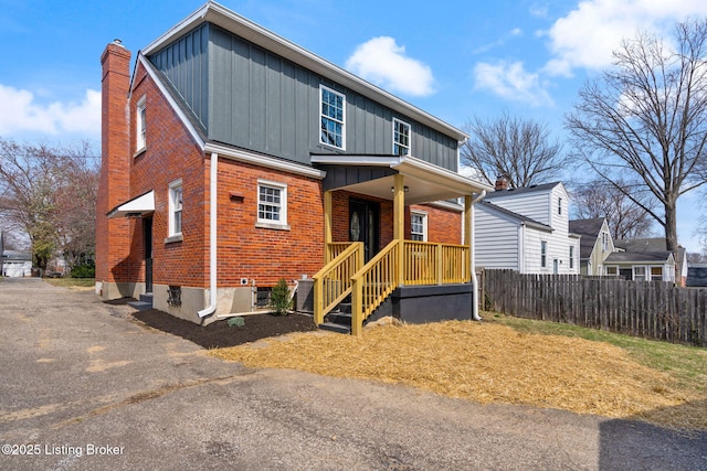 view of front of house featuring brick siding, board and batten siding, a chimney, and fence