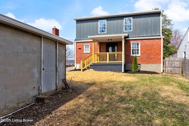 back of house featuring brick siding, a lawn, board and batten siding, and fence