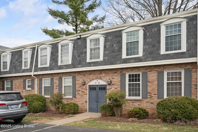 multi unit property featuring brick siding, mansard roof, and roof with shingles