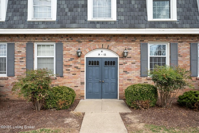 entrance to property featuring mansard roof and brick siding