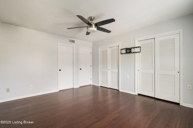 unfurnished bedroom featuring visible vents, two closets, a ceiling fan, dark wood-style floors, and baseboards