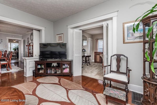 living room featuring visible vents, a textured ceiling, baseboards, and wood finished floors