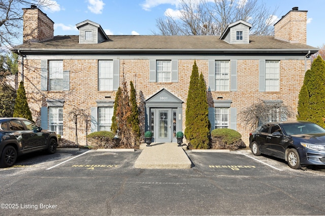 view of front of home with uncovered parking, brick siding, and a chimney