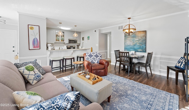 living room featuring an inviting chandelier, visible vents, dark wood-style flooring, and ornamental molding