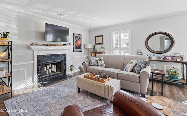 living room featuring a textured ceiling, wood finished floors, a high end fireplace, crown molding, and a decorative wall