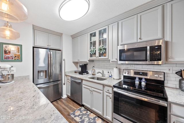 kitchen with a sink, tasteful backsplash, stainless steel appliances, glass insert cabinets, and dark wood-style flooring