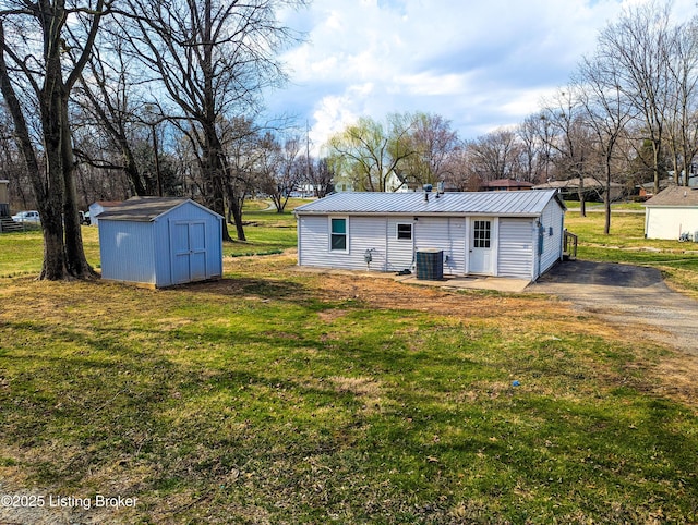 rear view of house featuring central AC unit, a lawn, metal roof, an outbuilding, and a storage unit