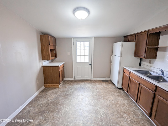 kitchen with open shelves, baseboards, light countertops, freestanding refrigerator, and a sink