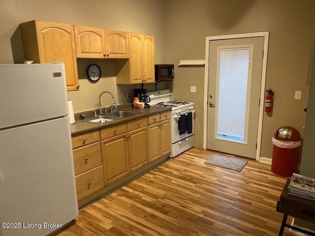 kitchen with white appliances, light brown cabinets, a sink, light wood-style floors, and dark countertops