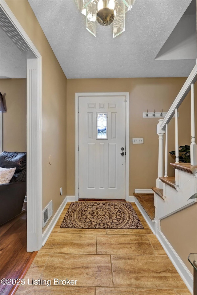 entryway with visible vents, stairway, a textured ceiling, and an inviting chandelier