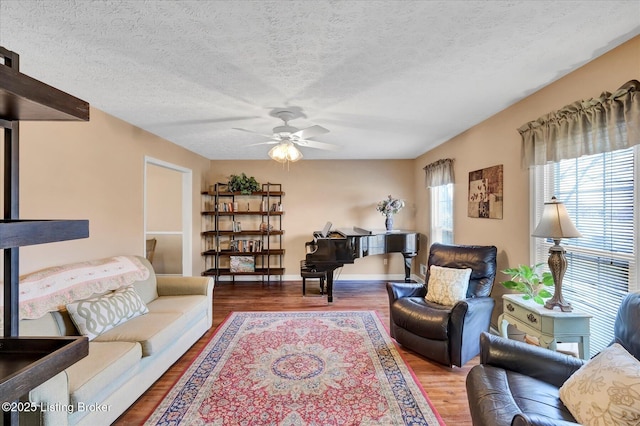 living area with baseboards, a textured ceiling, wood finished floors, and a ceiling fan