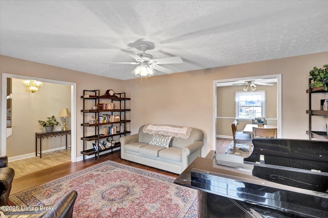 living room with baseboards, a textured ceiling, ceiling fan, and wood finished floors