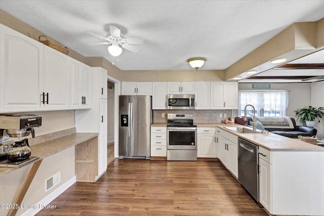 kitchen with a peninsula, dark wood-style floors, white cabinets, stainless steel appliances, and a sink