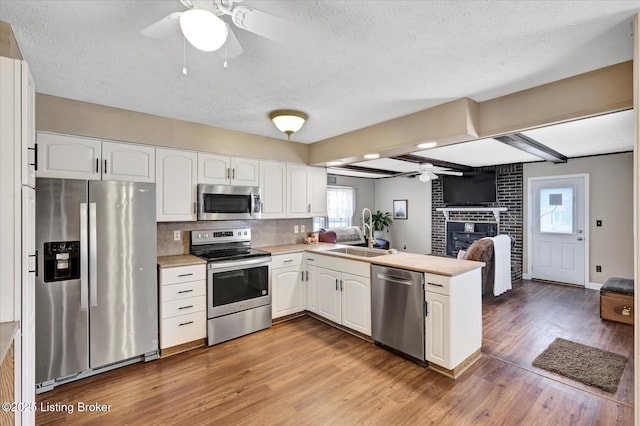 kitchen with a peninsula, a fireplace, a sink, ceiling fan, and appliances with stainless steel finishes