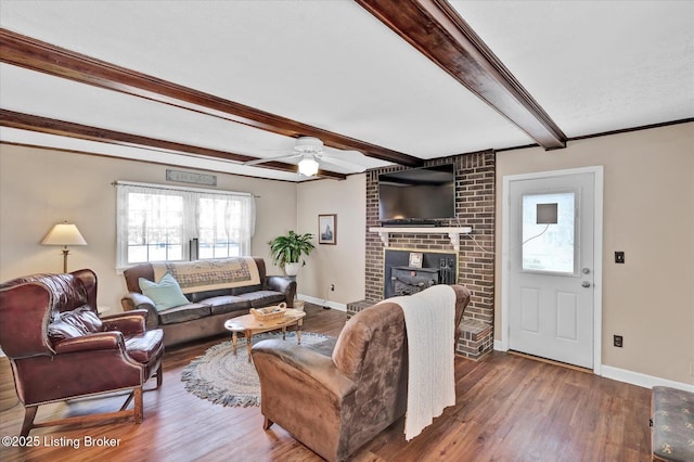 living area featuring baseboards, beamed ceiling, a fireplace, wood finished floors, and a ceiling fan