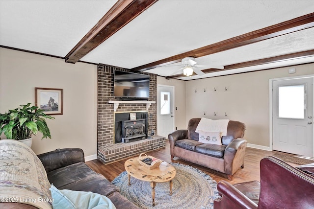 living area featuring beam ceiling, a ceiling fan, wood finished floors, baseboards, and a wood stove