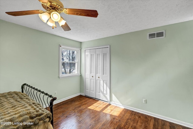 unfurnished bedroom featuring wood finished floors, visible vents, baseboards, a closet, and a textured ceiling