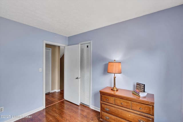 bedroom featuring a closet, a textured ceiling, baseboards, and wood finished floors