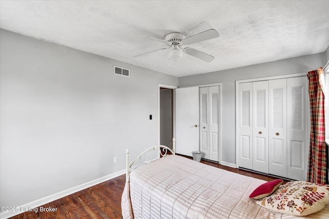 bedroom featuring visible vents, multiple closets, a textured ceiling, wood finished floors, and baseboards