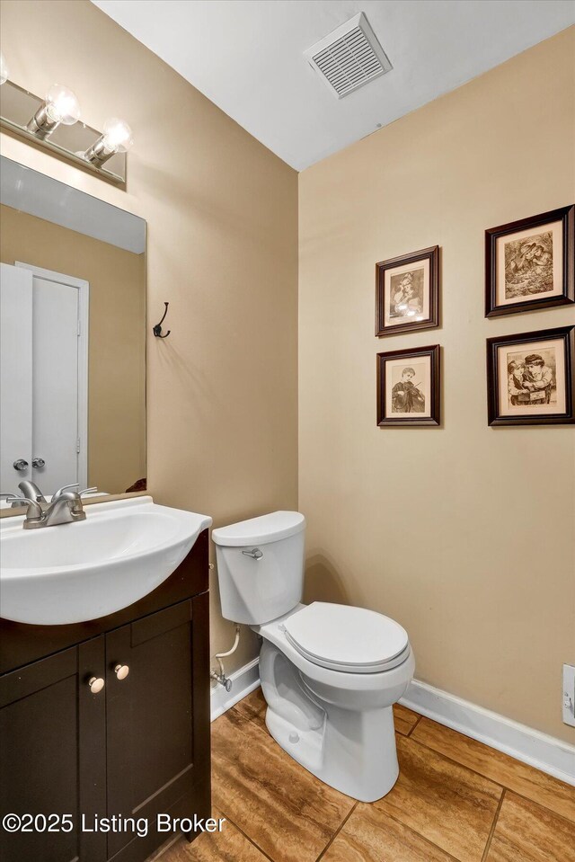 half bathroom featuring visible vents, baseboards, toilet, and vanity