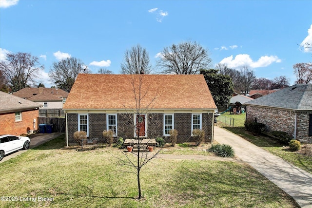 view of front of home featuring brick siding, a shingled roof, a front lawn, and fence