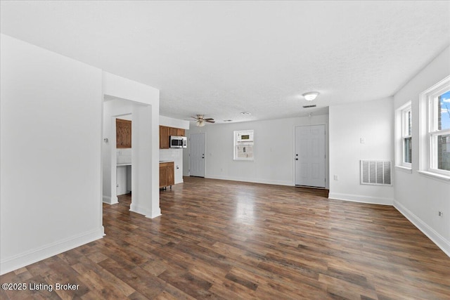 unfurnished living room featuring visible vents, ceiling fan, baseboards, a textured ceiling, and dark wood-style flooring