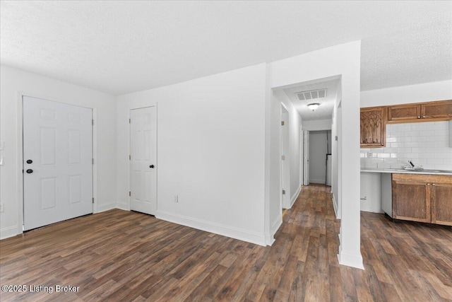 unfurnished living room with dark wood-style floors, visible vents, a textured ceiling, and a sink