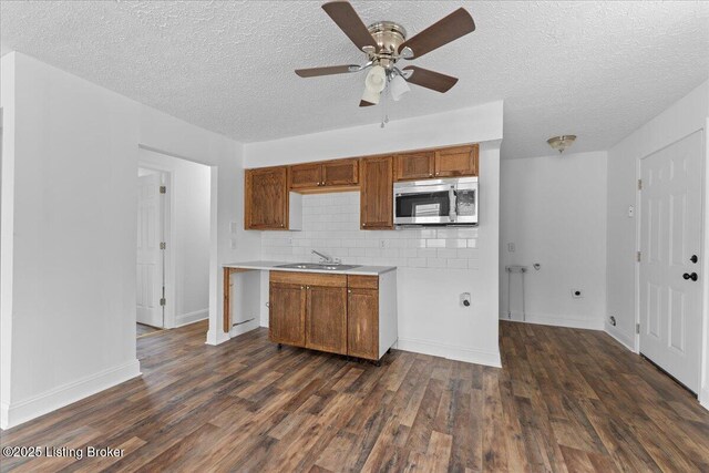 kitchen featuring stainless steel microwave, brown cabinets, dark wood-type flooring, and a sink