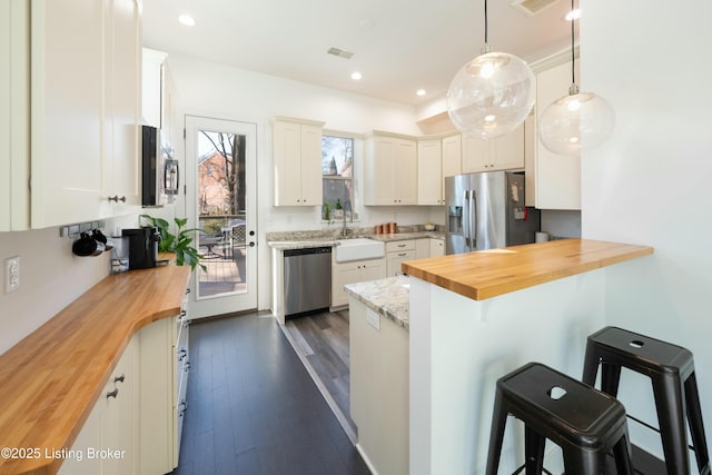 kitchen with a sink, stainless steel appliances, butcher block countertops, and a breakfast bar area