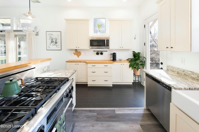 kitchen with dark wood-style flooring, butcher block countertops, hanging light fixtures, white cabinets, and appliances with stainless steel finishes