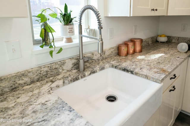 room details featuring white cabinets, light stone countertops, and a sink