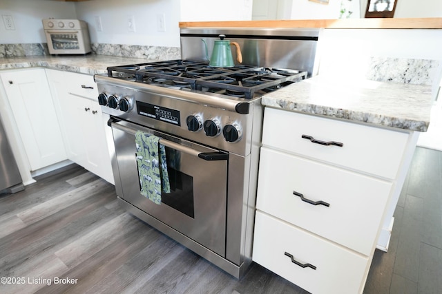 kitchen with light stone counters, high end stainless steel range oven, dark wood-style floors, and white cabinetry