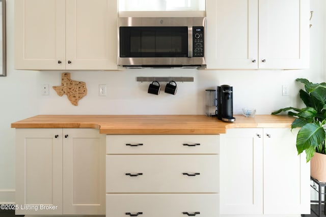 kitchen with butcher block countertops, white cabinets, and stainless steel microwave