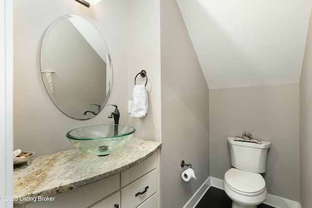 half bath featuring vanity, lofted ceiling, toilet, and baseboards